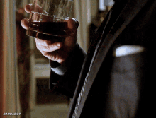 a man in a suit and tie holds a glass of whiskey in his right hand