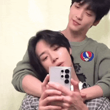 a man is holding another man 's head while taking a selfie with his phone .