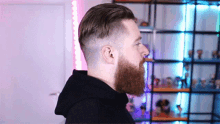 a man with a beard and a shaved head is standing in front of a shelf filled with figurines .