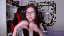 a woman wearing glasses and headphones is making a heart shape with her hands while sitting in a red chair .