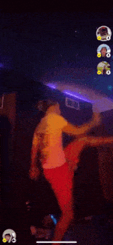 a man in a yellow shirt and red shorts is dancing in a dark room with purple lights .