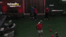 a man in a red shirt is kicking a soccer ball in front of a tv reality sign