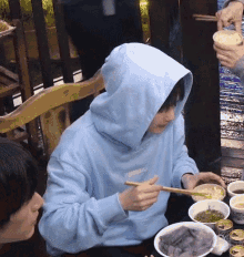 a person wearing a blue hoodie is eating noodles with chopsticks