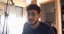 a man with a mustache is sitting in front of a microphone in a room .