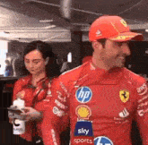 a man and a woman are standing next to each other wearing red ferrari shirts .