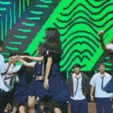 a group of people in school uniforms are dancing on a stage in front of a green background .