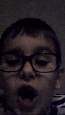 a young boy wearing glasses with his mouth open .