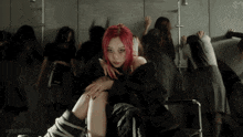 a woman with red hair is sitting in a chair in front of a group of dancers