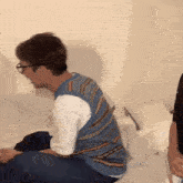 a man is sitting on a bed wearing glasses and a striped vest .