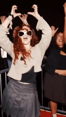 a woman wearing sunglasses holds her hands in the air