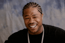 a man with braided hair and a beard is smiling