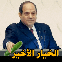 a man in a suit and tie is holding a cucumber in front of a podium with arabic writing