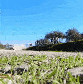 a car is driving down a dirt road with people standing on the side of the road