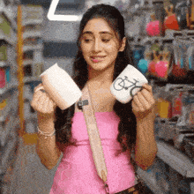 a woman in a pink tank top is holding two mugs in her hands .