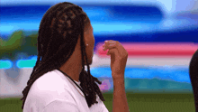 a man with dreadlocks wearing a white shirt is covering his mouth with his hand