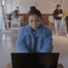 a woman in a blue jacket is typing on a laptop computer