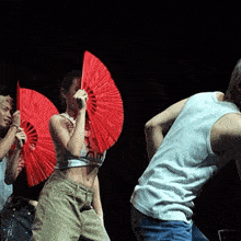 a woman in a white tank top is holding a red fan in her hand