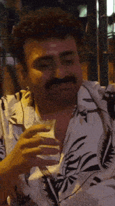 a man with a mustache is drinking from a glass while wearing a floral shirt .