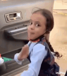 a little girl wearing headphones is standing in the back of a car making a funny face .