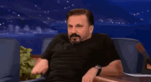 a man with a beard is sitting in a chair with his hands on his hips .