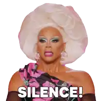 a drag queen with a huge white wig and a pink dress says silence