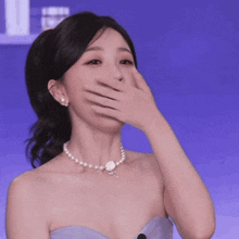 a woman with a pearl necklace covering her mouth with her hand
