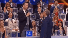 a man in a suit is talking into a microphone in front of a crowd with a sign that has the number 4 on it