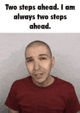 a bald man in a red shirt with the words two steps ahead i am always two steps ahead