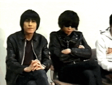 two men in leather jackets are sitting next to each other with their arms crossed .