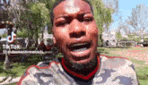 a man in a camouflage shirt is making a funny face while standing in a park .