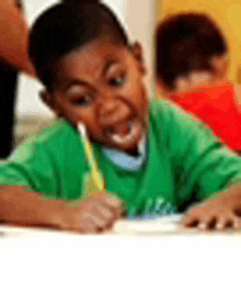 a young boy in a green shirt is sitting at a table writing on a piece of paper .