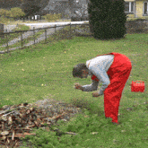 a man in red overalls is bending over in a grassy field
