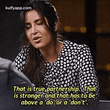 a woman in a black and white polka dot shirt is sitting at a table with a quote .