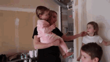 a woman is holding a little girl in her arms while a boy and two girls look on .