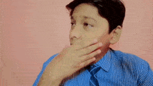 a young boy in a blue striped shirt and tie covering his mouth with his hand