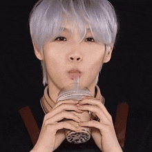 a person with white hair is drinking from a plastic cup with a straw