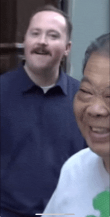 a man with a mustache is smiling next to another man with a white shirt