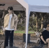 a man in a yellow jacket is standing under a white tent .