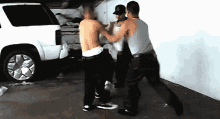three men are fighting in front of a white suv in a parking garage
