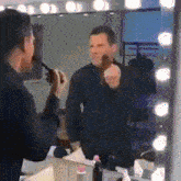 a man is applying makeup in front of a mirror with lights