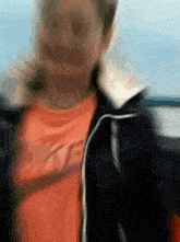 a blurry picture of a person wearing an orange shirt and black jacket