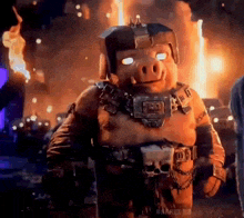 a pig with a helmet on is standing in front of a burning city .