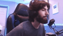 a man with a beard is sitting in a chair in front of a microphone and headphones .