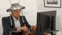 a man in a suit is sitting in front of a computer wearing a metal hat .