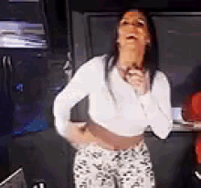 a woman in a white crop top and floral pants is standing in a kitchen .