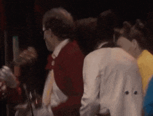 a group of people are standing in a dark room and one of them is wearing a red jacket and tie .