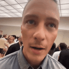 a man in a denim shirt looks at the camera in a crowded room