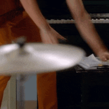 a man in orange pants is playing a cymbal in front of a piano