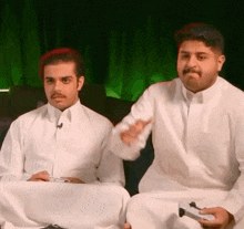 two men are sitting next to each other and playing a video game .