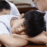 a young man is sleeping on a desk in a classroom